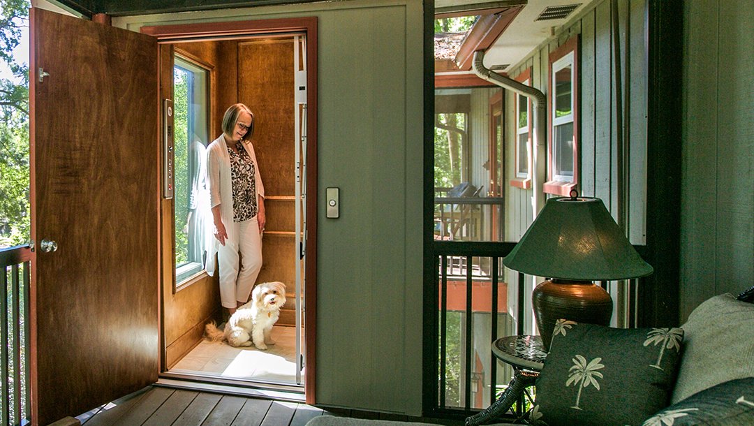 Woman standing in a home elevator with a small dog at her feet