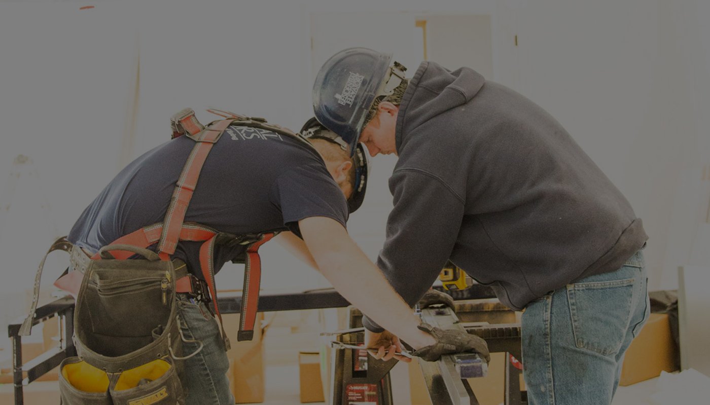 Two workers wearing safety gear collaborate on a construction task.