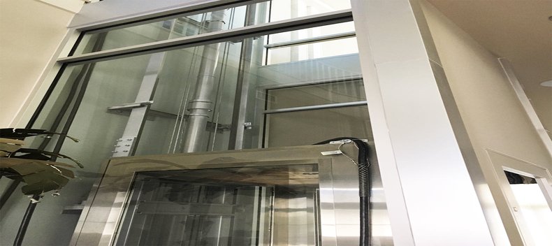 Glass-walled residential elevator shaft with visible mechanical components