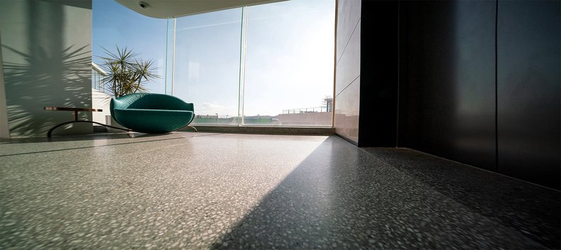 Sunlit modern room with terrazzo floor and a teal chair by large windows