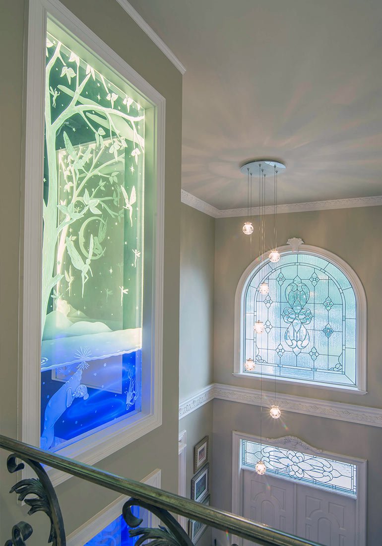 Glass panel on a home elevator shaft beside an ornate upstairs landing