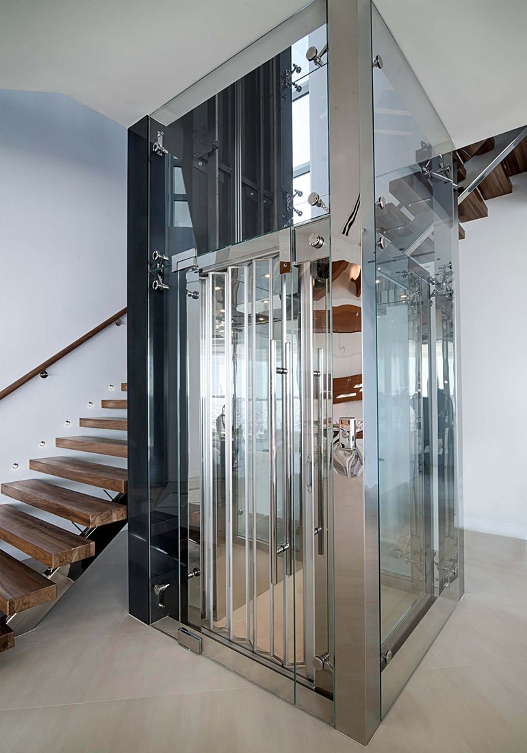 Glass home elevator with metal accordion doors beside wooden stairs