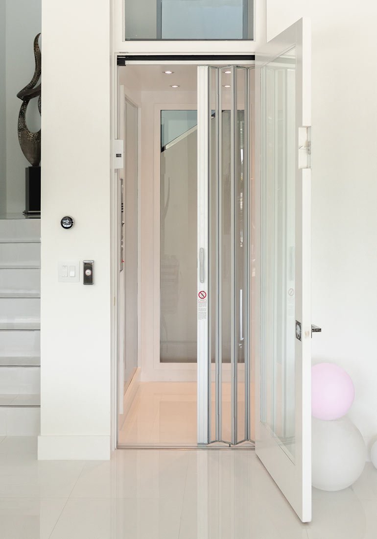 Modern home elevator with glass accordion doors in a bright white interior.