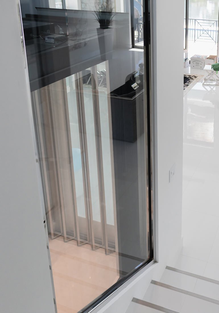 Glass elevator shaft view showing an elevator with vertical panel doors inside a modern home