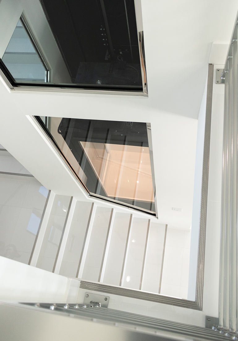 Looking down a white stairwell beside a glass elevator shaft
