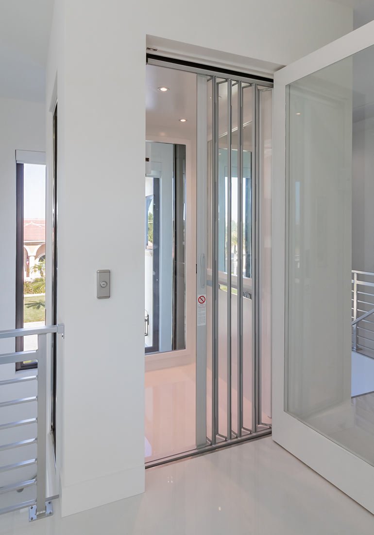 Modern home elevator with slim metal accordion doors in a bright white hallway