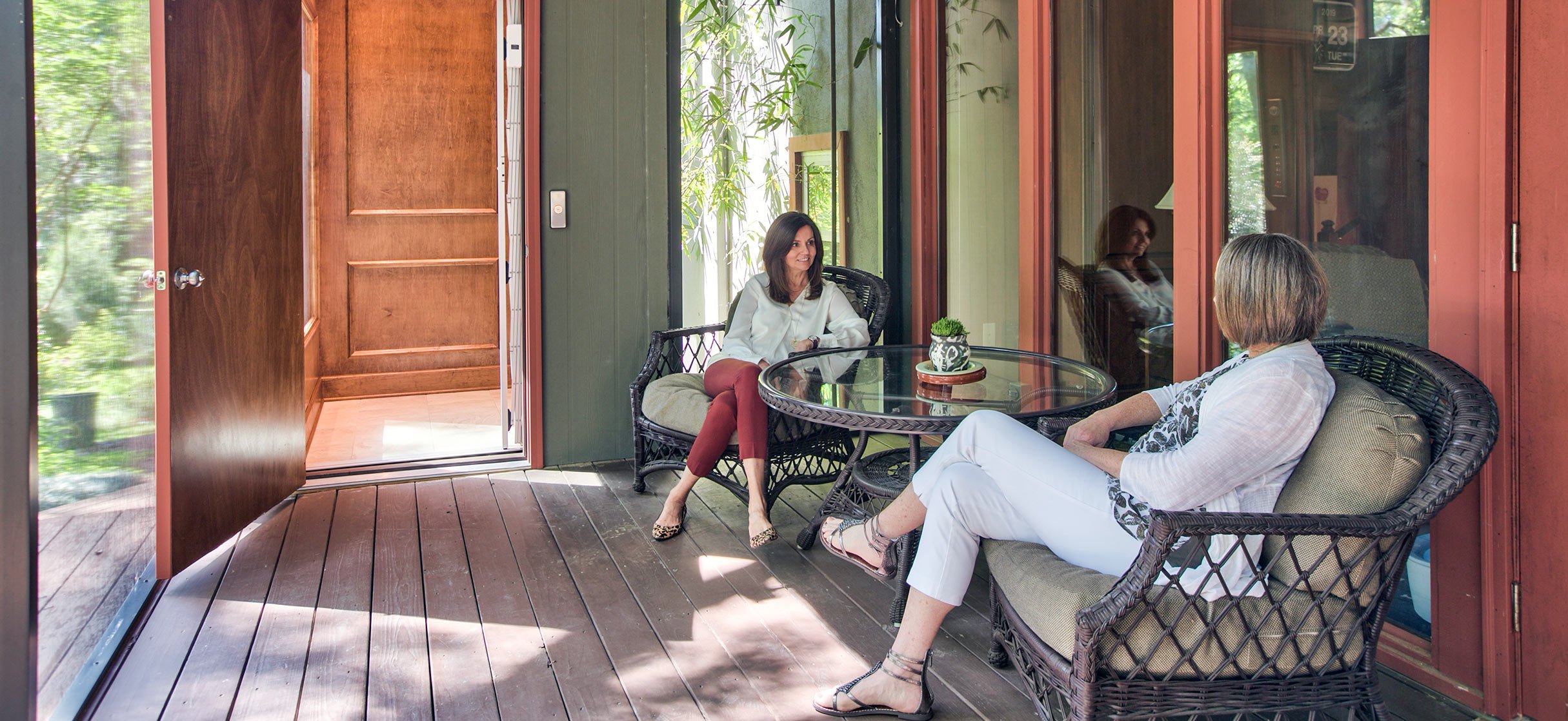 Two women sitting on a patio with an open wooden elevator door nearby
