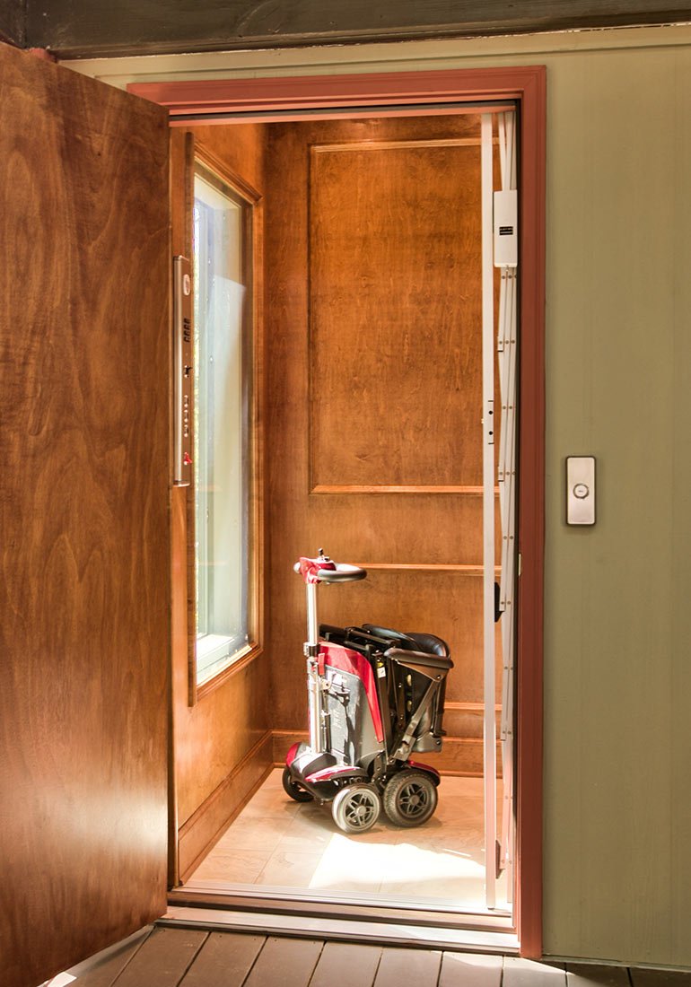 Home elevator with wood paneling containing a folded mobility scooter