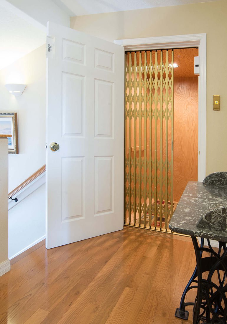 Home elevator with a gold accordion gate behind an open white door