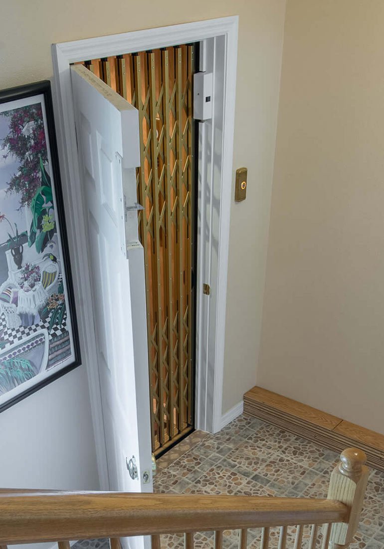 Gold accordion gate inside a home elevator viewed from the top of a staircase