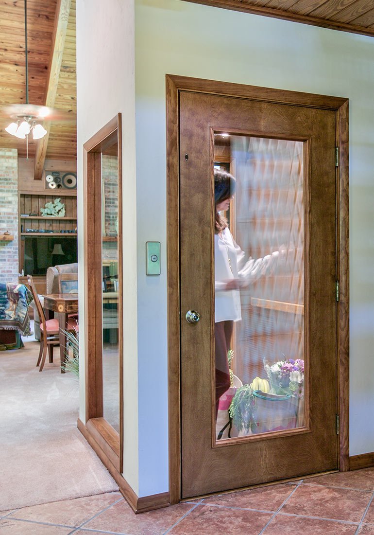 Woman inside a small home elevator with a wooden door and glass panel
