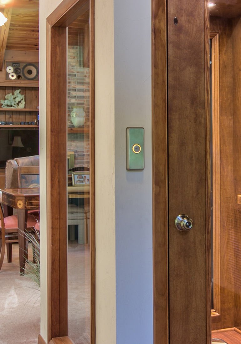 Close-up of a home elevator’s wooden door and wall-mounted call button
