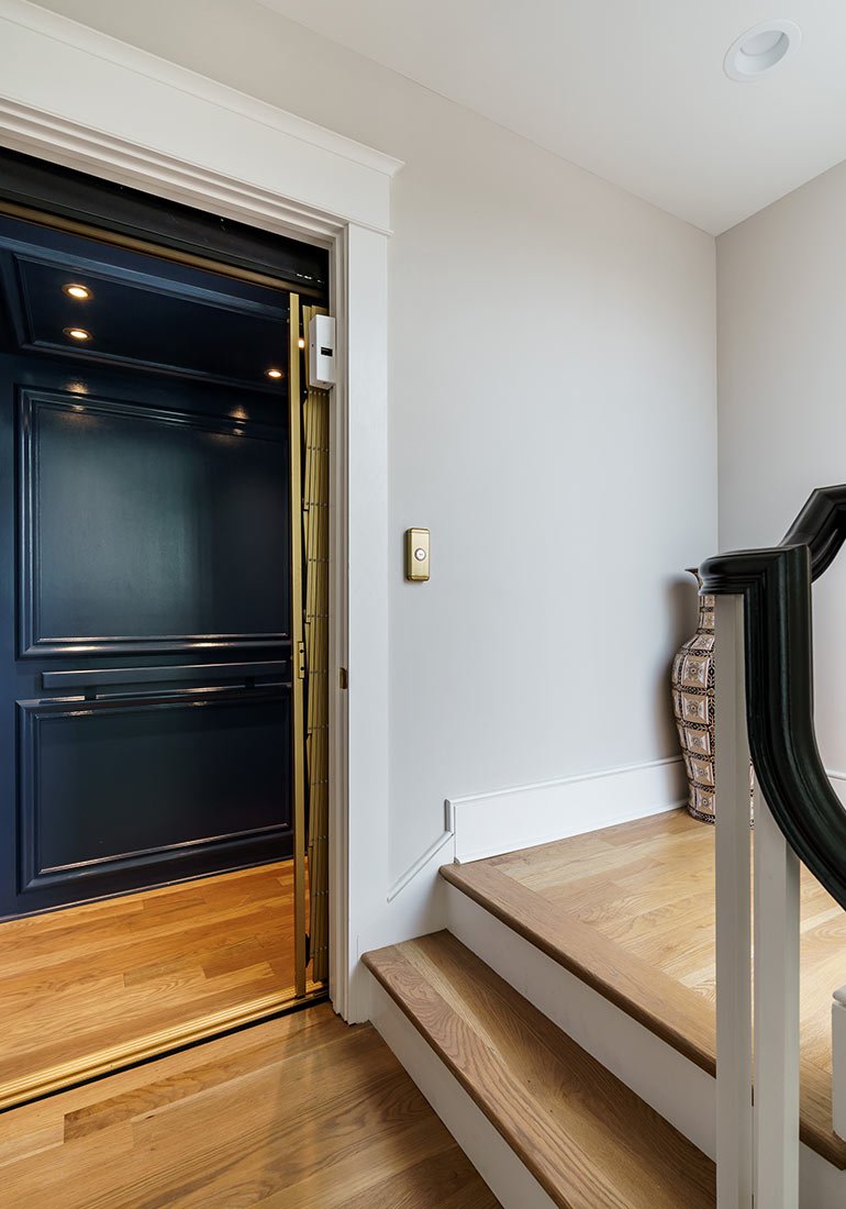 Open home elevator beside a wooden staircase