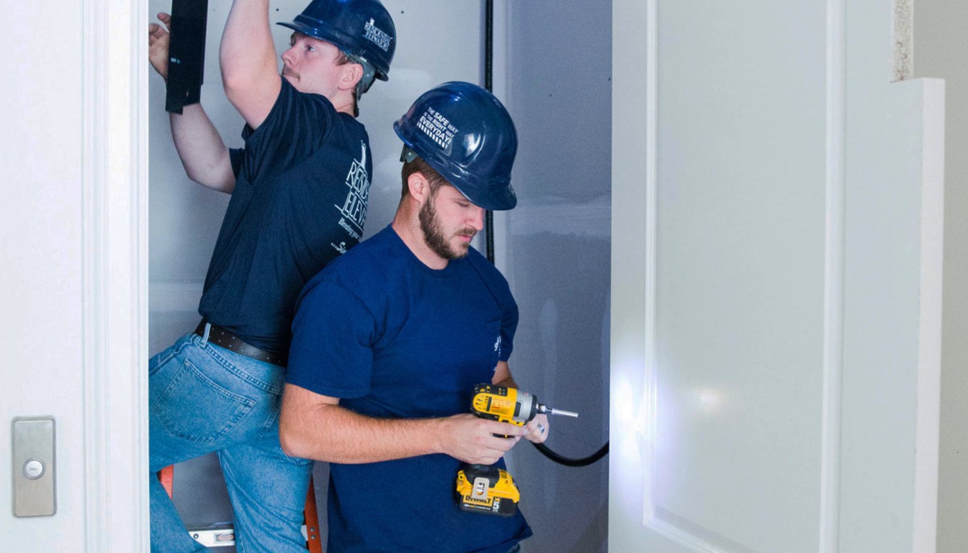 Two men wearing hard hats working in a small space